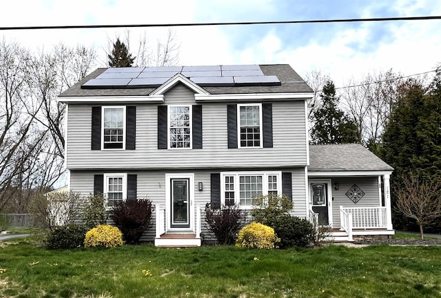 colonial inspired home featuring a front lawn, solar panels, and a shingled roof