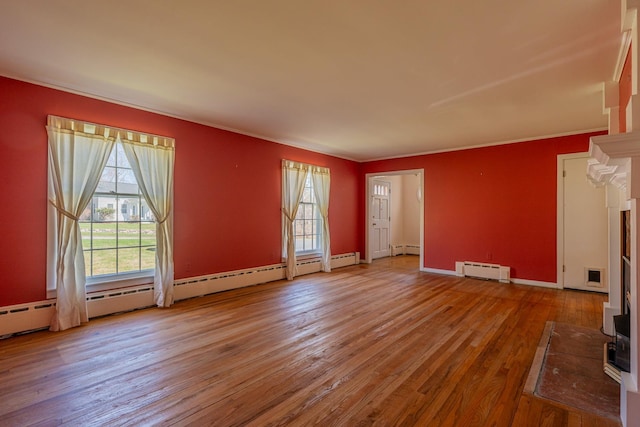 unfurnished living room with hardwood / wood-style flooring, crown molding, and a baseboard heating unit