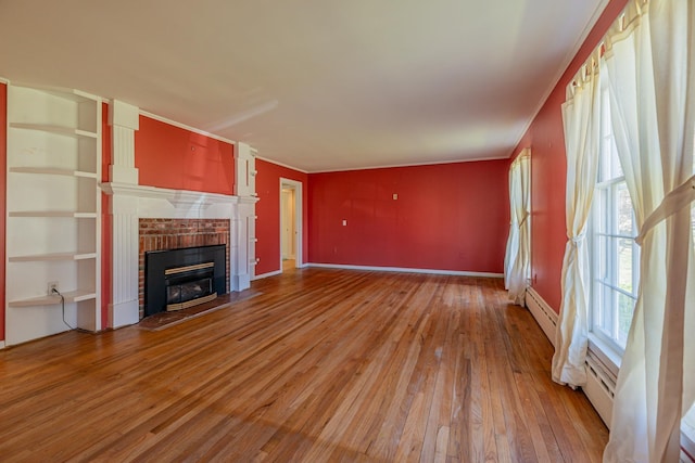 unfurnished living room with light wood-style floors, baseboards, a baseboard heating unit, and a brick fireplace