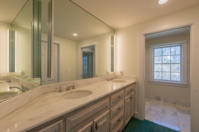 full bath featuring double vanity, marble finish floor, and a sink