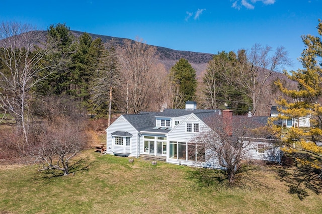 back of property with a lawn, a mountain view, roof with shingles, and a chimney