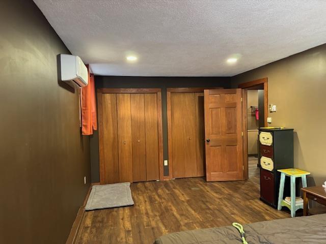 bedroom featuring a textured ceiling, multiple closets, recessed lighting, a wall unit AC, and dark wood-style floors