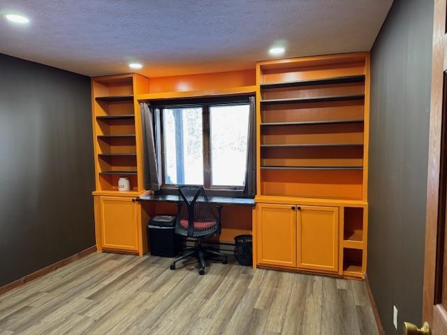 office space featuring a textured ceiling, built in desk, baseboards, recessed lighting, and light wood-style flooring