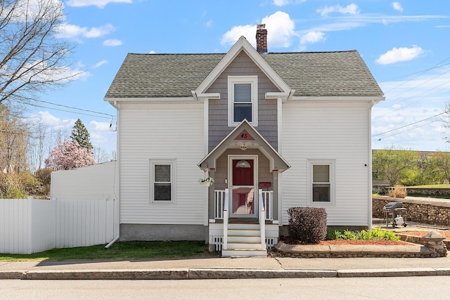 traditional home featuring fence, a chimney, and a shingled roof