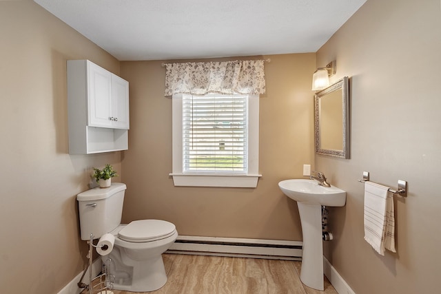 bathroom with wood finished floors, baseboard heating, toilet, a sink, and baseboards