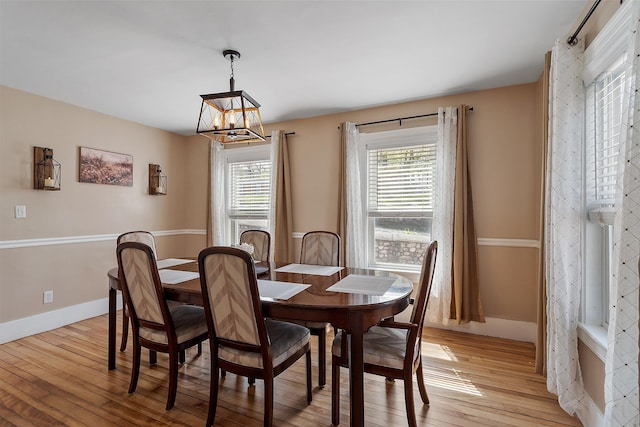 dining area with baseboards, an inviting chandelier, and light wood finished floors
