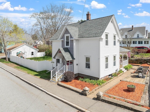 traditional-style house featuring a residential view, fence, a chimney, and roof with shingles