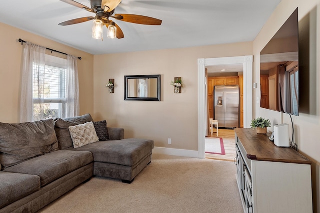living room with baseboards, a ceiling fan, and light carpet