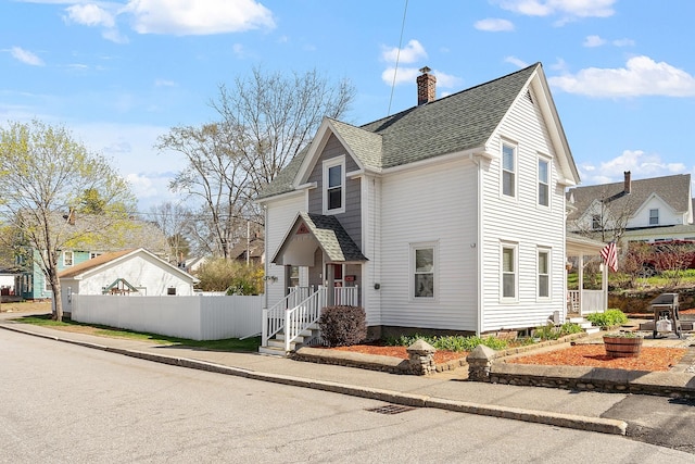 view of front facade featuring a chimney, fence, and a shingled roof