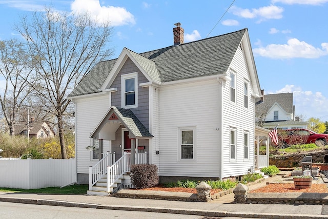 traditional-style house with a chimney, fence, and a shingled roof