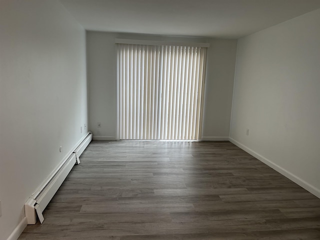 spare room featuring a baseboard heating unit, wood finished floors, and baseboards