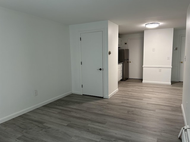 spare room featuring baseboards, wood finished floors, and a baseboard heating unit