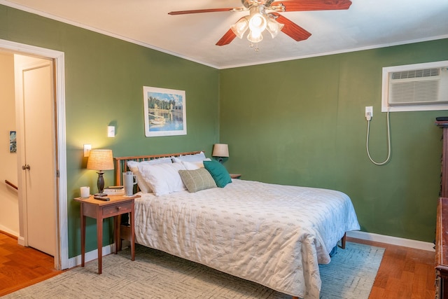 bedroom featuring baseboards, ornamental molding, an AC wall unit, wood finished floors, and a ceiling fan