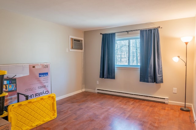 interior space featuring baseboard heating, baseboards, a wall unit AC, and wood finished floors