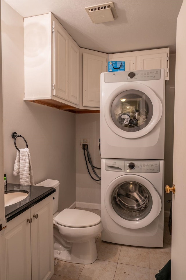 bathroom featuring visible vents, stacked washing maching and dryer, toilet, vanity, and tile patterned flooring