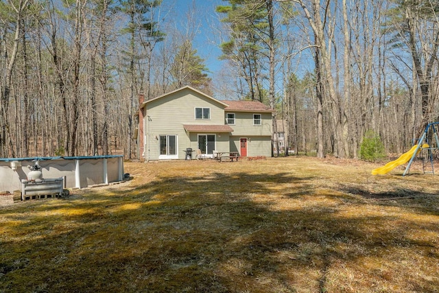 back of property featuring a chimney, a yard, a playground, and an outdoor pool