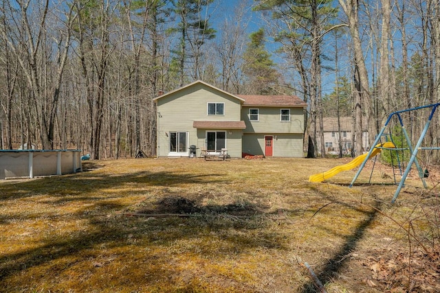 rear view of property featuring a lawn, an outdoor pool, and a playground