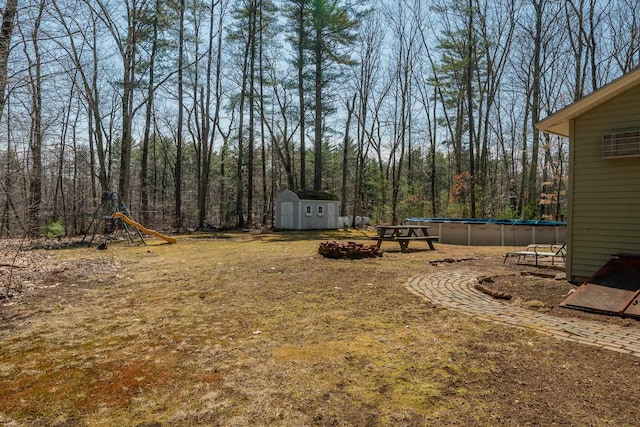 view of yard featuring an outdoor structure, a shed, an outdoor pool, and a view of trees