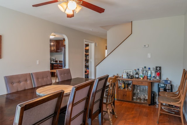 dining area featuring arched walkways, ceiling fan, wood finished floors, and a dry bar