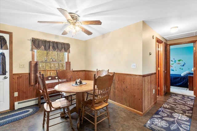 dining area featuring baseboard heating, wainscoting, a ceiling fan, and wood walls