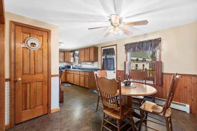 dining room with wood walls, dark floors, ceiling fan, baseboard heating, and wainscoting