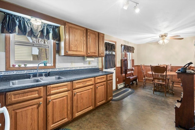 kitchen with wainscoting, brown cabinets, baseboard heating, dark countertops, and a sink