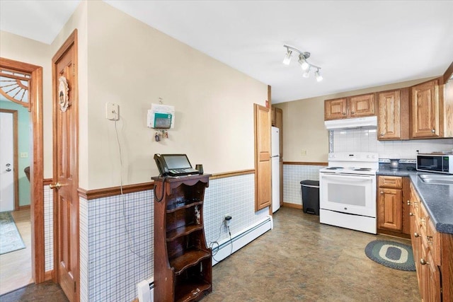 kitchen with under cabinet range hood, a wainscoted wall, white appliances, dark countertops, and a baseboard radiator