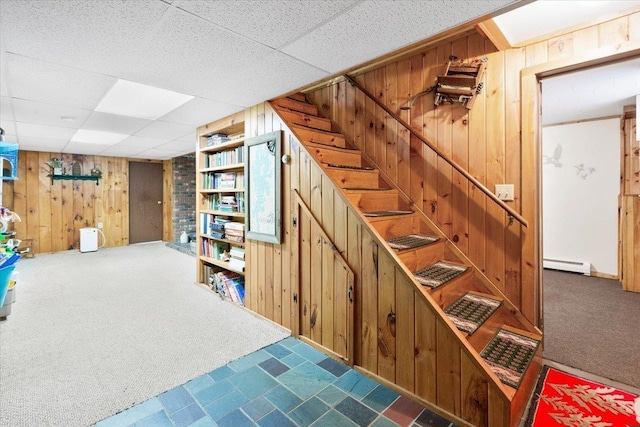 finished basement featuring wood walls, stairs, a baseboard heating unit, and carpet floors