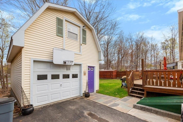 view of side of property featuring fence, aphalt driveway, a wooden deck, a lawn, and a gambrel roof