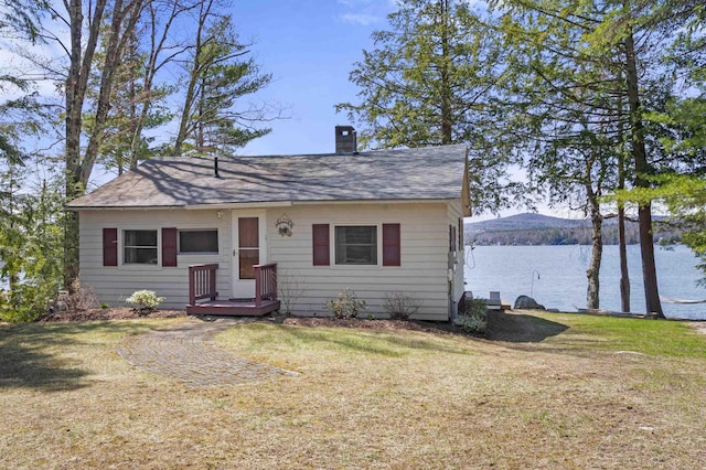 view of front of property with a front lawn, roof with shingles, a water view, and a chimney