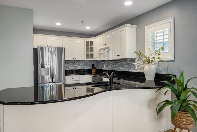 kitchen with tasteful backsplash, a sink, stainless steel refrigerator with ice dispenser, a peninsula, and white microwave
