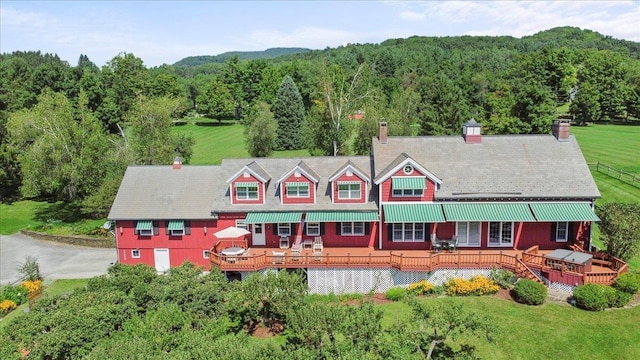 rear view of house featuring a lawn, a deck, a chimney, and a wooded view