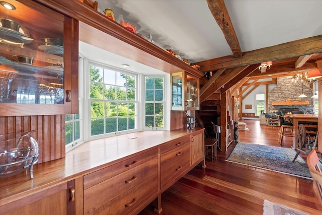 interior space featuring dark wood-style floors, brown cabinetry, beamed ceiling, and a stone fireplace