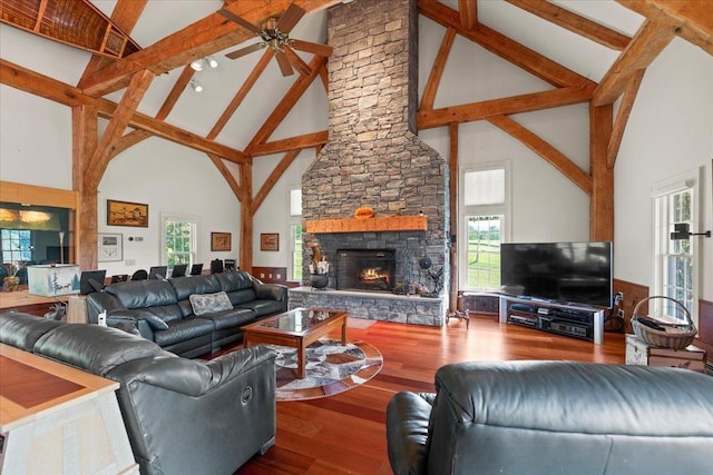 living area featuring wood finished floors, a stone fireplace, beam ceiling, high vaulted ceiling, and a ceiling fan