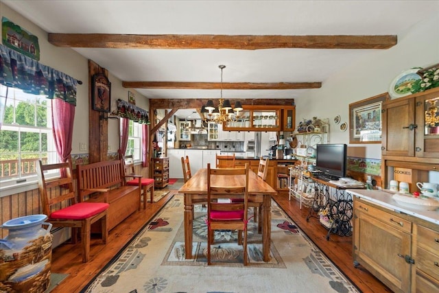dining area featuring light wood finished floors, a notable chandelier, and beam ceiling