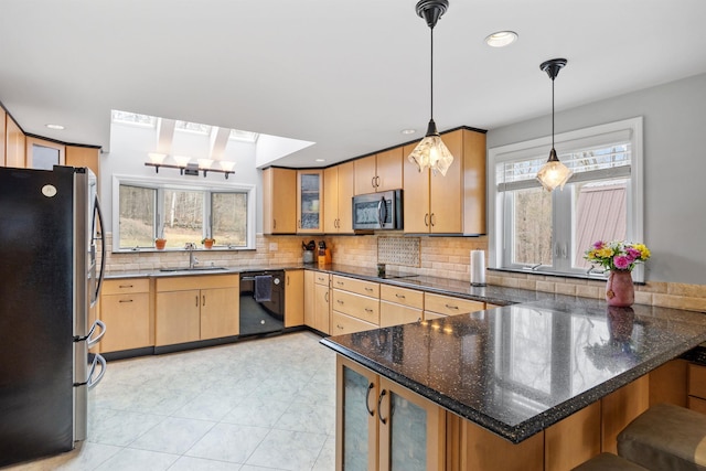 kitchen with black appliances, a peninsula, plenty of natural light, and a sink