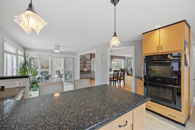 kitchen featuring dark stone counters, light brown cabinetry, dobule oven black, pendant lighting, and a ceiling fan
