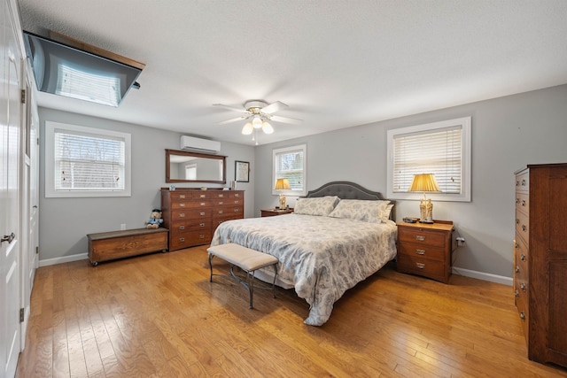 bedroom featuring baseboards, a wall unit AC, a ceiling fan, and light wood-style floors