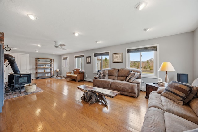 living area with a wood stove, light wood finished floors, ceiling fan, and baseboard heating