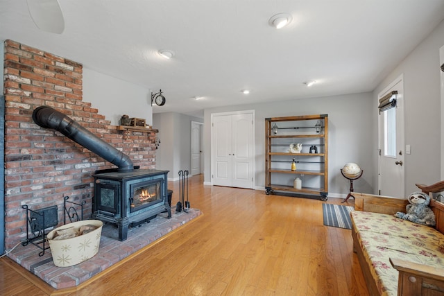 living area with a wood stove, recessed lighting, wood finished floors, and baseboards
