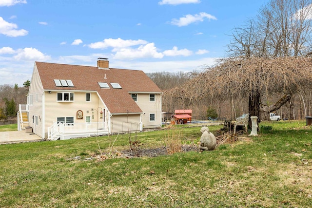 back of house with a chimney, a patio area, a yard, and roof with shingles