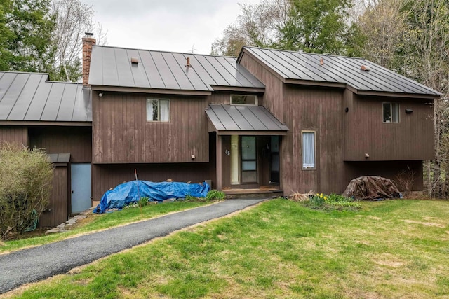 back of house with a lawn, metal roof, a chimney, and a standing seam roof