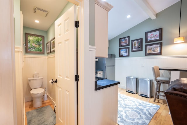 bathroom with visible vents, wood finished floors, a wainscoted wall, lofted ceiling with beams, and toilet