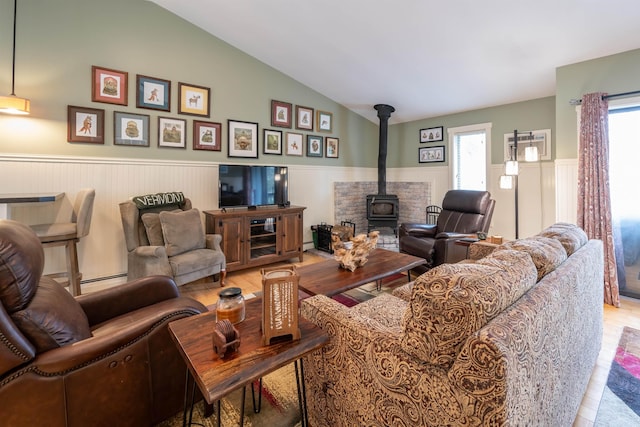 living room with wainscoting, a wood stove, wood finished floors, and lofted ceiling