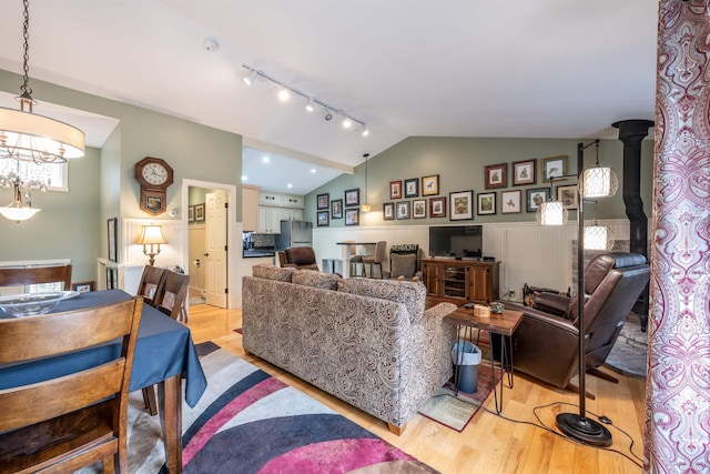 living room with an inviting chandelier, track lighting, a wood stove, light wood finished floors, and vaulted ceiling