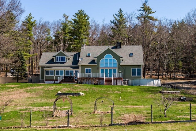 back of property with a shingled roof, a wooden deck, a swimming pool, and a yard