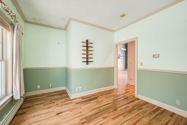 empty room featuring crown molding, baseboards, wood finished floors, and a baseboard radiator