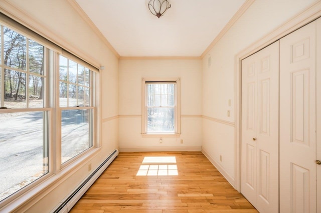 empty room with a healthy amount of sunlight, a baseboard heating unit, crown molding, and light wood finished floors