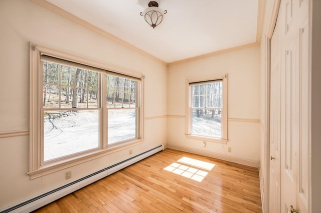 unfurnished room featuring baseboard heating, ornamental molding, light wood finished floors, and plenty of natural light
