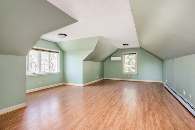 additional living space featuring a baseboard heating unit, baseboards, an AC wall unit, vaulted ceiling, and wood finished floors